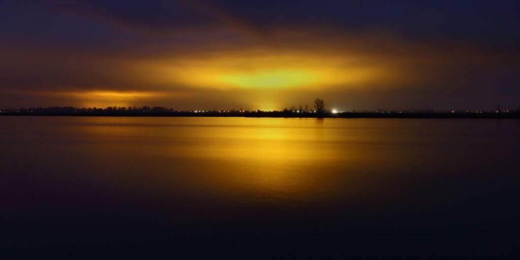 See bei Sonnenuntergang mit goldenen Lichtern am Horizont