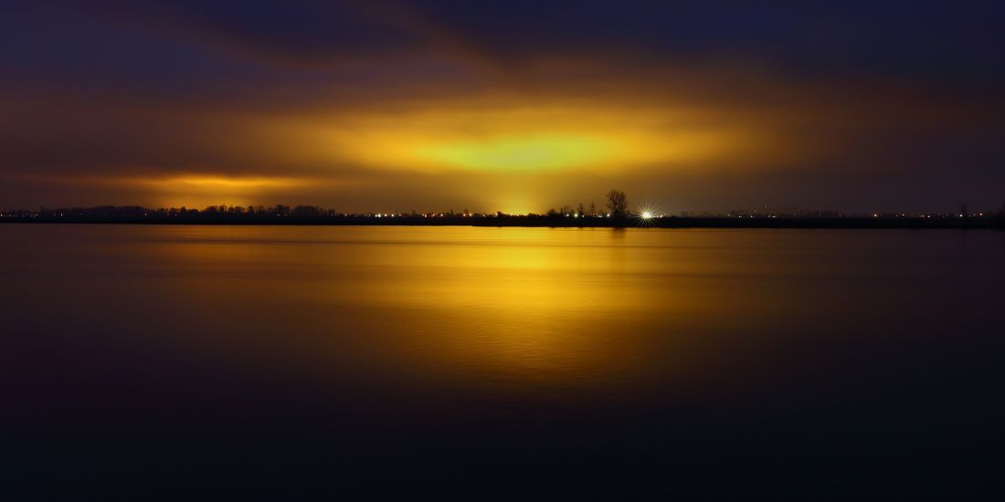 See bei Sonnenuntergang mit goldenen Lichtern am Horizont